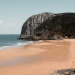 brown sand beach near brown rocky mountain under blue sky during daytime